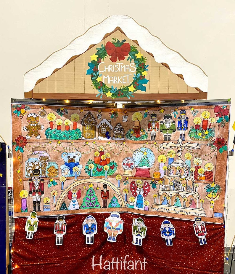 May include: A hand-painted backdrop depicting a Christmas market scene with a gingerbread house, nutcrackers, and a snow globe. The backdrop is decorated with lights and a wreath that says "Christmas Market". The bottom of the backdrop has the word "Hattifant" written in cursive.