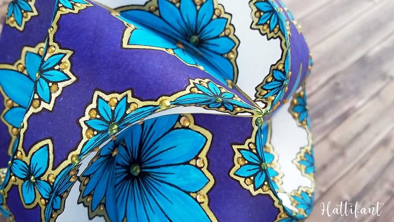 May include: A close-up of a folded paper ornament with a blue and gold floral pattern. The ornament is made of paper and has a 3D effect.