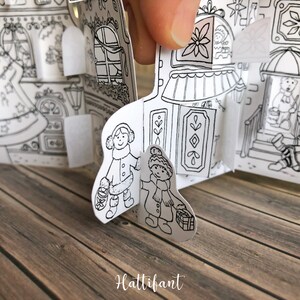 May include: Black and white illustration of a Christmas village scene with two children wearing winter clothes and carrying gifts. The illustration is part of a pop-up book.