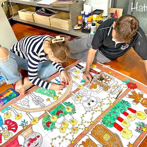 May include: A large, white, paper tablecloth with a Christmas theme. The tablecloth is decorated with gingerbread houses, candy canes, and other festive imagery. A girl and a man are coloring the tablecloth with markers.