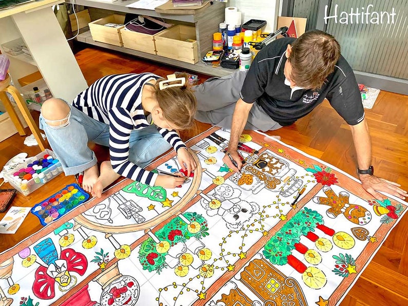 May include: A large, white, paper tablecloth with a Christmas theme. The tablecloth is decorated with gingerbread houses, candy canes, and other festive imagery. A girl and a man are coloring the tablecloth with markers.