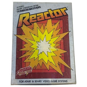 May include: A rectangular video game cartridge box for Reactor by Parker Brothers. The cover features a large yellow and orange starburst graphic against a dark red background. Text includes A VIDEO GAME CARTRIDGE FROM PARKER BROTHERS, Arcade Game Series, and FOR ATARI & SEARS VIDEO GAME SYSTEMS.