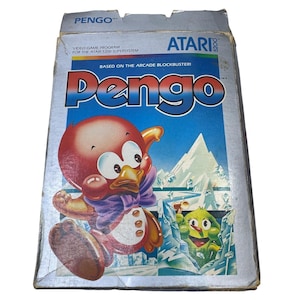 May include: A vintage Atari 5200 video game box for the game Pengo. The silver box features the title Pengo in large blue and red letters, a red penguin character with a purple bowtie, and a green creature amidst blue ice blocks and mountains.