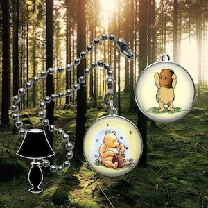 May include: A Winnie the Pooh fan pull chain with two round, colourful images. One image shows Winnie the Pooh holding a pot of honey. The other image shows Winnie the Pooh holding a pot of honey over his head. The chain is silver and has a black lampshade in the background.