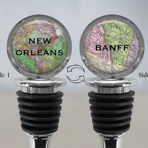May include: A silver bottle stopper with a black rubber stopper. One side features a vintage map of New Orleans, the other side features a vintage map of Banff.