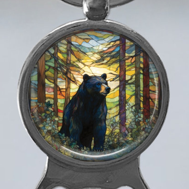 May include: A black bear stands in a woodland setting, surrounded by colourful stained glass trees. The bear is facing right and has a dark brown nose and black eyes. The stained glass background features a variety of colours, including blue, green, yellow, and orange.