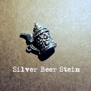 May include: A silver beer stein charm with intricate floral designs. The charm is a small, detailed replica of a traditional beer stein.
