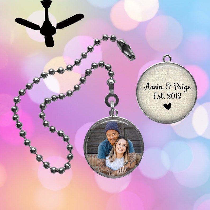 Op de afbeelding: Een ronde metalen trekketting voor een plafondventilator met een zilveren kralenketting en een ronde hanger. E&eacute;n kant toont een kleurenfoto van twee personen, terwijl de andere kant de tekst Arvin & Paige Est. 2012 met een klein zwart hartje bevat.