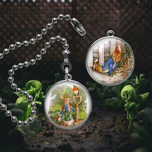 May include: Two Peter Rabbit themed fan pull charms. One charm features Peter Rabbit hiding behind a fence, the other charm features Peter Rabbit holding a carrot in a garden.
