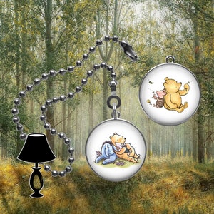 May include: A ceiling fan pull chain with two round charms featuring Winnie the Pooh characters. One charm shows Pooh and Piglet, the other shows Pooh and Eeyore. The chain has a black lamp charm.