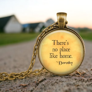 May include: A gold necklace with a round pendant featuring a yellow watercolor background and the quote "There's no place like home. ~Dorothy"