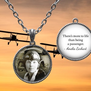 May include: A silver necklace with a round pendant featuring a black and white photo of Amelia Earhart. The other side of the pendant has the quote "There's more to life than being a passenger. - Amelia Earhart".