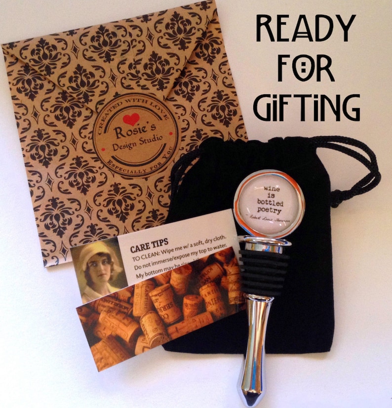 May include: A silver bottle stopper with a circular top featuring the text 'wine is bottled poetry' by Robert Louis Stevenson, a black drawstring pouch, a care instruction card with a vintage portrait, and a brown envelope with a damask pattern.