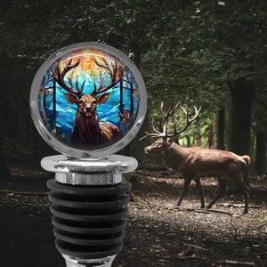 May include: A silver bottle stopper with a round, colorful stained glass design of a deer with antlers in a forest setting.