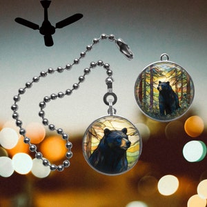 May include: A silver chain with a round glass pendant featuring a black bear in a forest setting. The pendant has a stained glass look with yellow, orange, and blue colors.