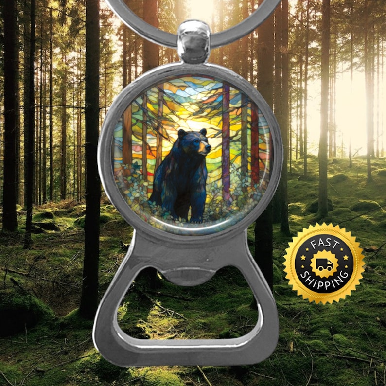 May include: A silver bottle opener keychain featuring a round, colourful stained glass image of a black bear standing in a forest. The image has a yellow, orange, blue and green colour scheme.