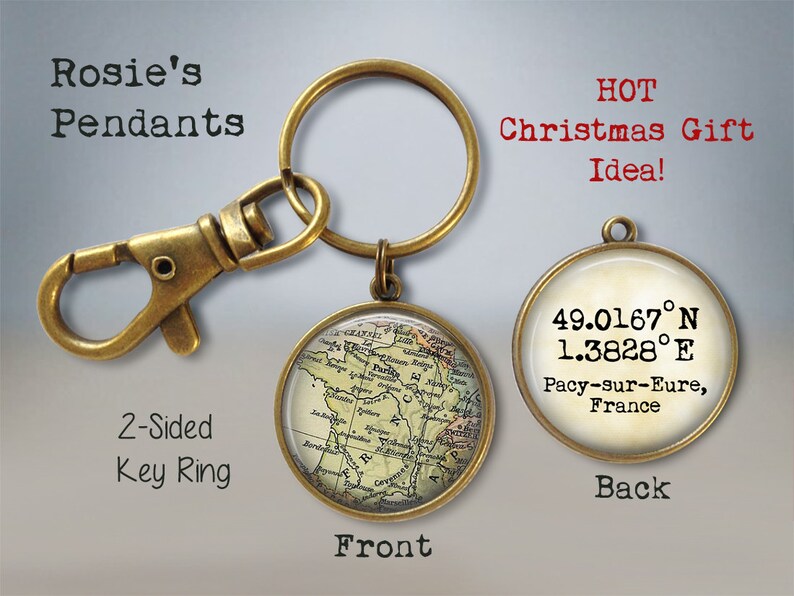 May include: A two-sided key ring with a map of France on one side and coordinates and the text "49.0167&deg;N 1.3828&deg;E Pacy-sur-Eure, France" on the other side. The key ring is made of brass and has a vintage look.