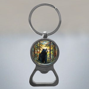 May include: A silver bottle opener keychain featuring a round, colourful image of a black bear standing in a forest. The image has a stained glass effect.