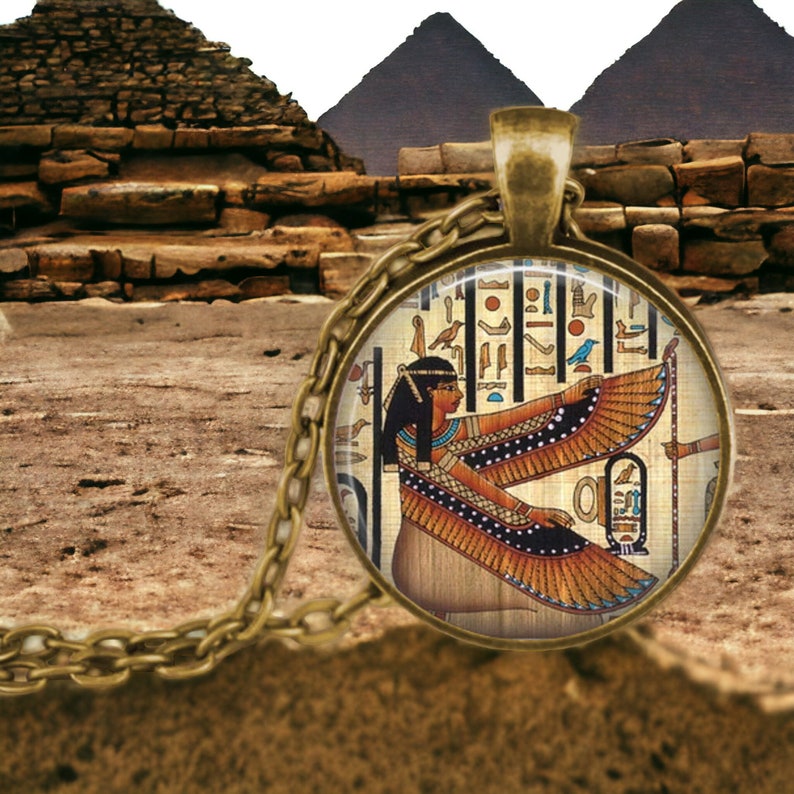 May include: A gold chain necklace with a round glass pendant featuring an image of an Egyptian goddess with wings. The pendant is surrounded by hieroglyphics.
