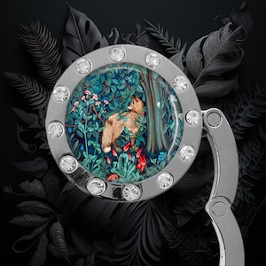 May include: A silver-toned metal purse hook with a round, clear, crystal-encrusted frame. The frame features a colorful image of a fox in a forest scene.