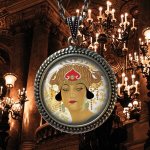 May include: A bronze pendant necklace featuring a round glass cameo with a portrait of a woman wearing a gold and red crown. The woman has dark hair and dark eyes and is wearing a gold and green necklace.