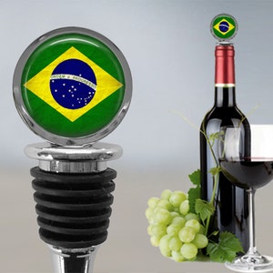 Op de afbeelding: Een zilveren flessenstop met een zwarte rubberen afdichting. De bovenkant van de stop heeft een cirkelvormig ontwerp met de Braziliaanse vlag. De vlag is groen, geel en blauw met een witte cirkel in het midden. De tekst "ORDEM E PROGRESSO" staat in wit op een blauwe band over het midden van de vlag.