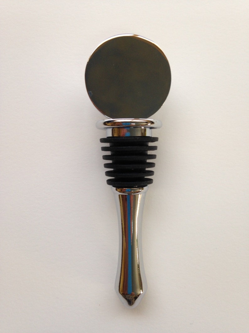 May include: A silver bottle stopper with a round, flat top and a black rubber stopper. The stopper is designed to fit into the neck of a wine bottle.