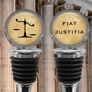 May include: Two silver bottle stoppers with black rubber stoppers. The top of each stopper features a round, cream-colored design. One design features a scale of justice and the other says "FIAT JUSTITIA".