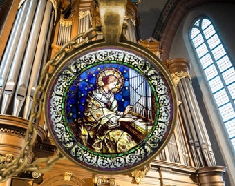 May include: A gold-toned pendant necklace with a round glass cameo featuring a stained glass image of a person playing a musical instrument. The cameo has a detailed ornate border with blue, green, and red accents. The background is a large pipe organ.
