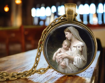 May include: A round pendant necklace with a bronze-colored chain. The pendant features a painting of a woman holding a baby and a lamb. The background is a blurred image of a church interior.