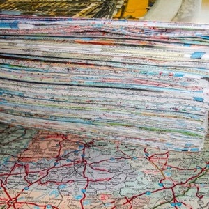 May include: A large stack of paper maps, likely road maps, with a colorful, detailed map visible underneath.
