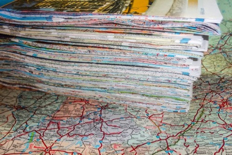 May include: A large stack of paper maps, likely road maps, with a colorful, detailed map visible underneath.