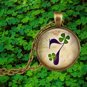 May include: A gold chain necklace with a round pendant featuring a vintage-style image of the number seven with three-leaf clovers. The pendant has a distressed, aged look.