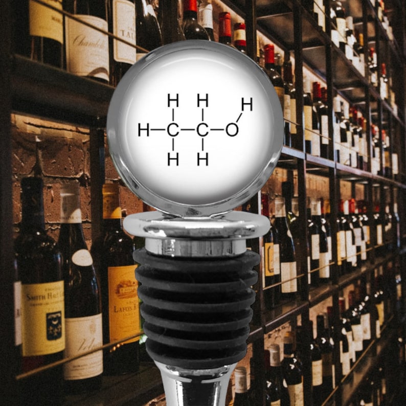 May include: A silver-toned bottle stopper featuring a circular top with a white insert displaying the black chemical structural formula for ethanol. The base consists of a tiered black rubber gasket designed for sealing wine bottles securely.