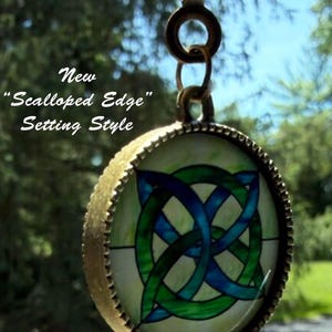 Op de afbeelding: Een ronde hanger met een blauw en groen Keltisch knoopontwerp in een bronskleurig metalen frame met een geschulpte rand. De hanger hangt aan een ronde ring. De tekst op de afbeelding luidt: New "Scalloped Edge" Setting Style.