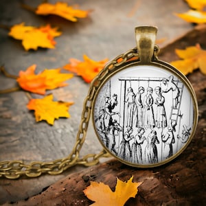May include: A bronze necklace with a round glass pendant featuring a black and white illustration of a historical execution scene. The illustration depicts several people hanging from a wooden structure, with others standing below.