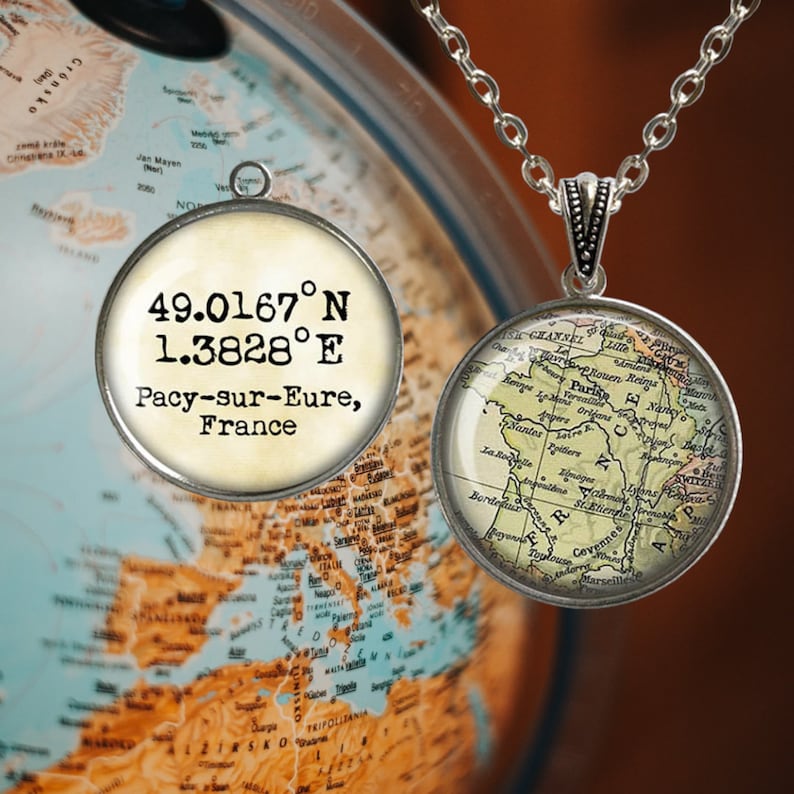 May include: A silver necklace with two round glass pendants. The top pendant has the coordinates 49.0167&deg;N 1.3828&deg;E and the text "Pacy-sur-Eure, France". The bottom pendant features a vintage map of France with the city of Paris highlighted.