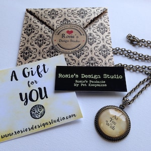 May include: A gift tag with the text "A Gift for You" and a website address. A brown paper envelope with a black and white pattern and a black and white business card with the text "Rosie's Design Studio" and the text "Rosie's Pendants My Pet Keepsakes". A gold necklace with a round pendant that says "As You Wish".