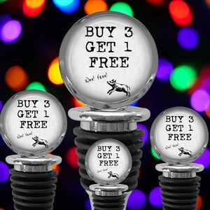 May include: Four silver-toned bottle stoppers with black rubber ribbed bases. Each circular top features the black text "BUY 3 GET 1 FREE" and "Wee! free!" above a small black illustration of a running pig, set against a white background.