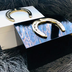 May include: Two wooden boxes with gold horseshoe accents. One box is white and the other is black with a wood grain pattern.