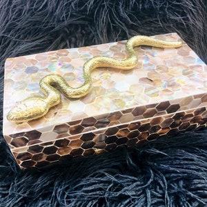 May include: A decorative box made of iridescent mother of pearl tiles in a honeycomb pattern. The box has a gold snake handle.