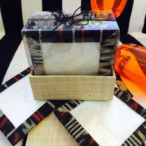 May include: Set of four coasters in a clear plastic box. The coasters are made of a natural material with a black and white striped pattern and a red accent. The box is tied with a black ribbon.