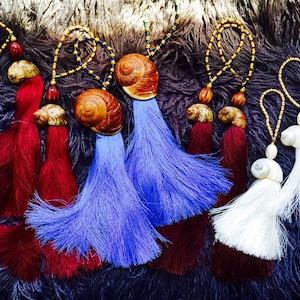 May include: Five colorful tassel keychains with seashells. The tassels are red, blue, and white. The seashells are brown and white.