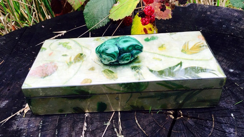 May include: A green malachite stone box with a floral design. The box is closed and has a green malachite stone knob.