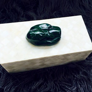May include: A white rectangular box with a green malachite stone on top. The box has a textured surface and the stone is smooth and polished.
