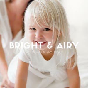 May include: A young girl with blonde hair smiles at the camera. She is wearing a white dress and is sitting on a white surface. The text "BRIGHT & AIRY" is superimposed on the image, along with the words "ADOBE CAMERA RAW PRESET".