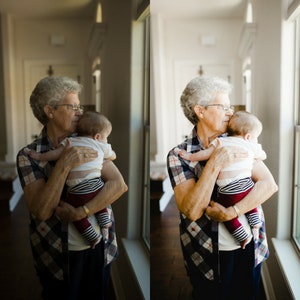Puede incluir: Una mujer con el pelo gris y gafas sostiene a un beb&eacute; en sus brazos. El beb&eacute; lleva una camisa blanca con rayas negras y rojas. La mujer lleva una camisa de cuadros y pantalones negros. El fondo es una pared de color claro con una ventana.