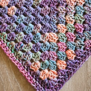 May include: A crocheted blanket with a square pattern in shades of purple, pink, blue, and green.