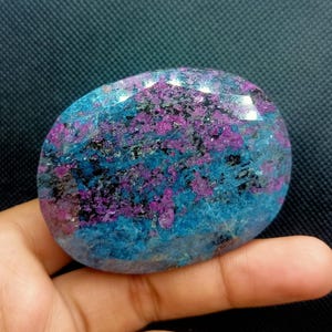 Peut inclure: Une grande pierre précieuse de forme ovale avec un motif de couleur bleu et violet. La pierre précieuse a une surface lisse et polie et est translucide.