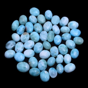 May include: A collection of oval-shaped, light blue gemstone cabochons. The stones have a cloudy, iridescent appearance.